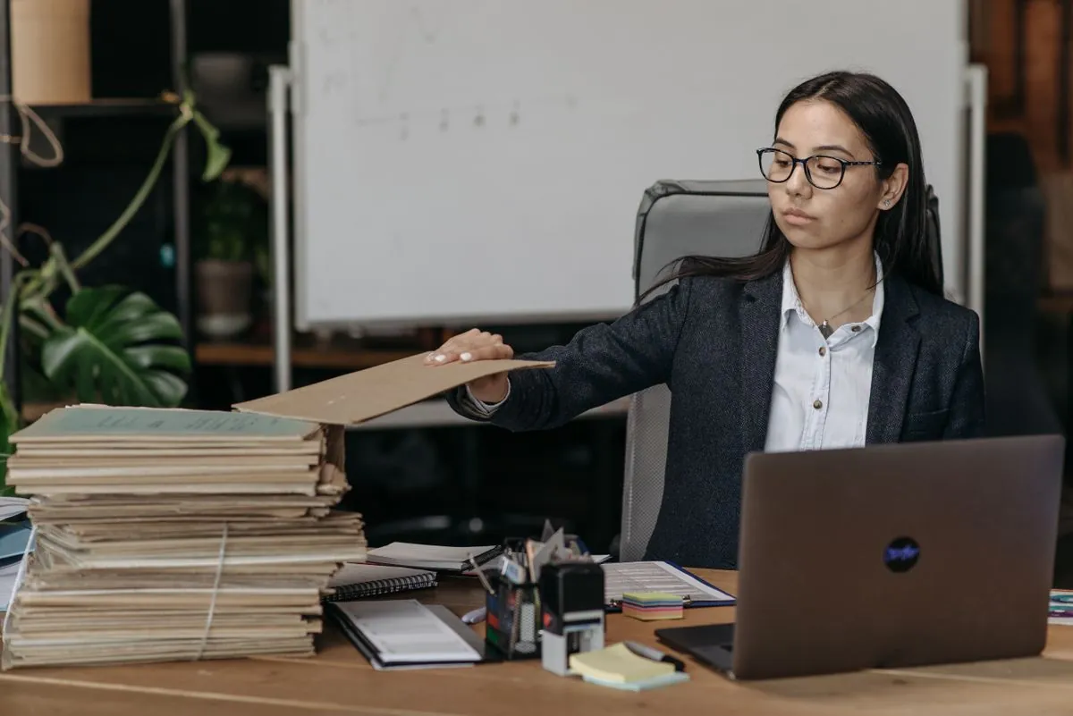 Mujer ordenando pilas de carpetas junto a su portátil