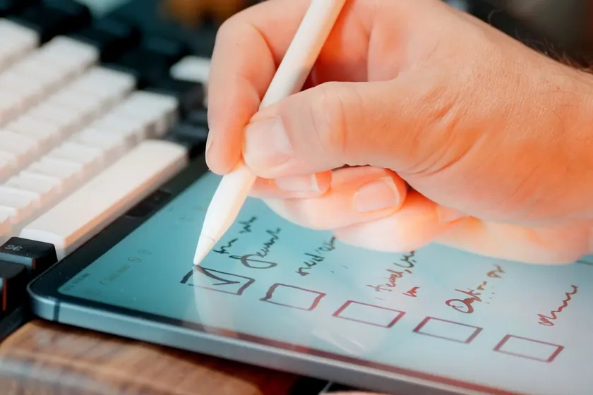 Mano con un lápiz digital marcando casillas en una tablet sobre una mesa de trabajo