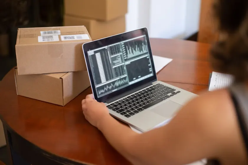 Persona frente a un portátil con gráficos, junto a varias cajas de pedidos sobre la mesa